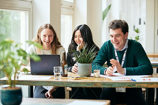 Three young people sitting at a table, laughing (image: Tübingen AI Center / Nino Strauch)