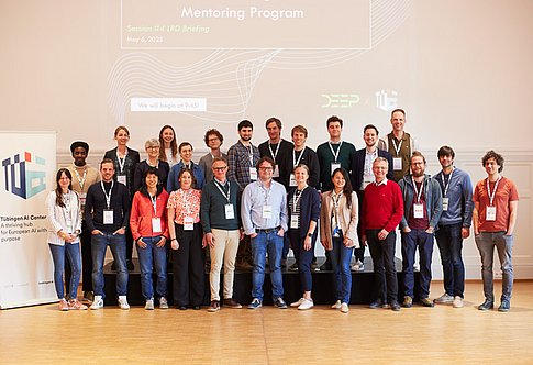 A group of people are standing in several rows on a stage. To the left is a Tübingen AI Center roll-up. Image: Nino Strauch / Tübingen AI Center