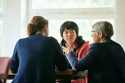 A group of three women sit at a table, bright windows in the background (image: Tübingen AI Center / Nino Strauch)